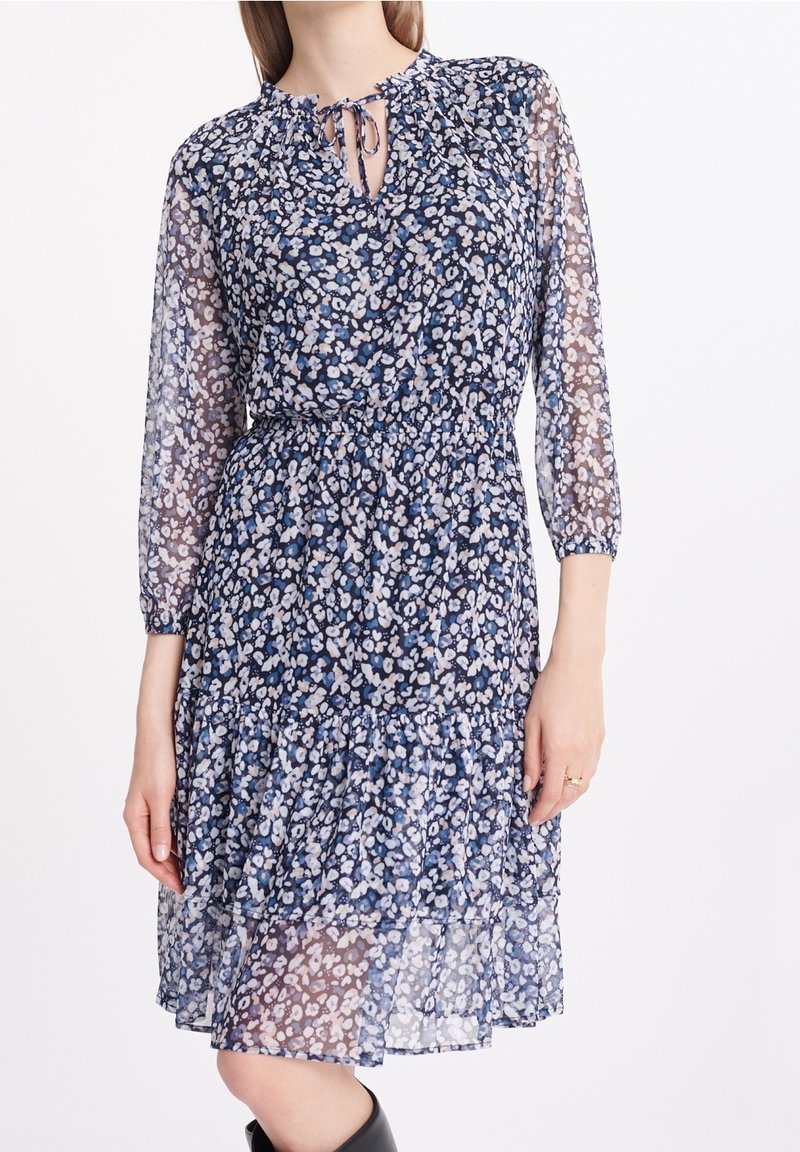 Blumenkleid mit navyfarbenem Hintergrund, ausgestattet mit transparenten langen Ärmeln, einem gebundenen Ausschnitt, elastischem Taillenband und geschichtetem Volant-Saum.