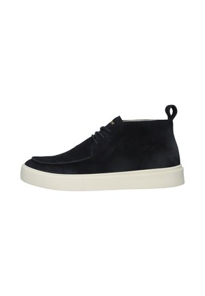 Zapatilla alta de ante negro con suela de goma blanca gruesa y cordones negros, vista de lado sobre un fondo blanco.