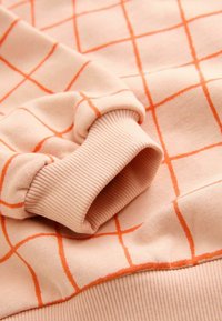 Světle růžová mikina s oranžovým mřížkovým vzorem, žebrovanými manžetami a měkkou texturovanou tkaninou s volným střihem.