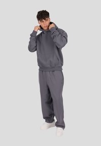 Szara bluza z kapturem i dopasowane spodnie dresowe, wykonane z miękkiego materiału. Kaptur jest regulowany, z przodu widoczna kieszeń. Całość dopełniają białe trampki.