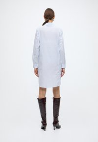 Lichtblauwe gestreepte overhemdjurk met lange mouwen, een kraag en een rechte snit, gecombineerd met glanzende bruine kniehoge stiletto laarzen.