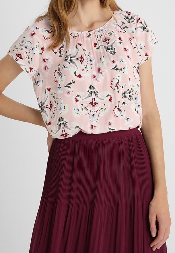 Blusa rosa a maniche corte con motivo floreale e scollatura arricciata, abbinata a una gonna plissettata bordeaux. Tessuto testurizzato in colori tenui.