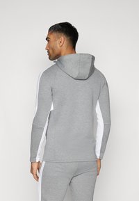 Grå sweatshirt med hætte og hvide sidelapper, lavet af blødt stof med en tætsiddende pasform. Glat tekstur og enkle linjer.