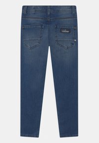 Modré džínové kalhoty s dvěma zadními kapsami, černou značkovou nášivkou na pravé kapse a viditelným prošíváním na bílém pozadí.