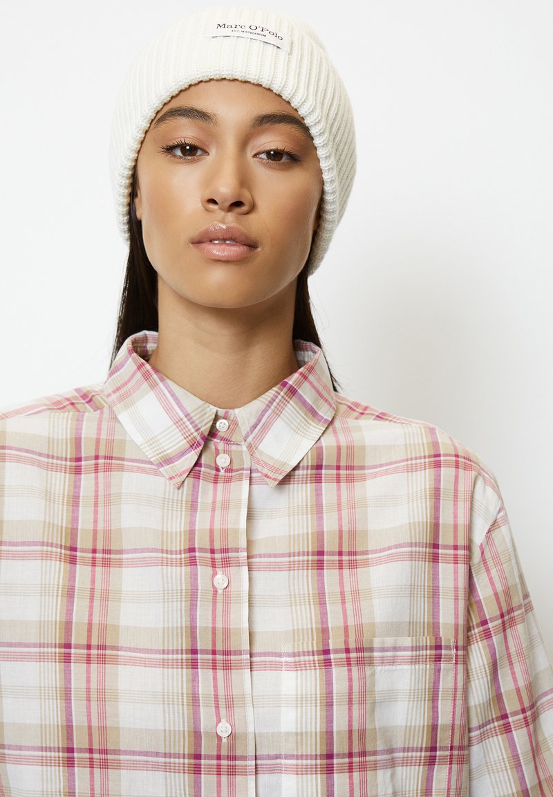 Geruite shirt in tinten van roze, beige en wit. Met een button-down kraag en een borstzakje. Een geribbelde witte beanie op het hoofd.