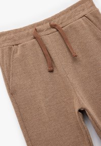 Brune joggers med struktureret overflade, der har et herringbone-mønster, elastisk talje med brunt snøre og sidelommer. Glat stoffinish.