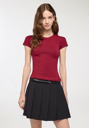 T-shirt corto color bordeaux abbinato a una gonna plissè nera. Presenta un colletto rotondo e una vestibilità slim, con una cintura nera che accentua il punto vita.