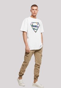 White t-shirt with multicolored graphic featuring a stylized "S" logo, paired with beige cargo pants and white sneakers. Casual fit.