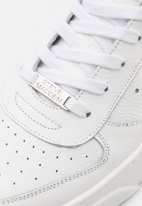 Bijele tenisice s kožnim gornjim dijelom, perforiranim detaljima i srebrnim logotipom "STEVE MADDEN" na jeziku, ravne bijele vezice.