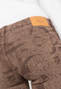 Bruna kordjeans med ett subtilt mönster, en bakficka och en tan läderlapp med märkningen "BDG" vid midjan.