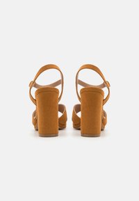 Brune semskede høye hælsandaler med kraftig blokkheel, ankelstropp og åpen tå-design. Teksturert finish og justerbar spenne.