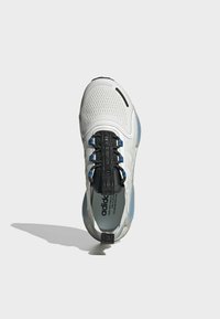 Vitt atletiskt sko med mesh-överdel, svarta skosnören med blå accenter, tjock sula och tydlig märkning på tungan och hälen.