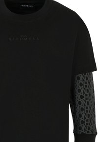 T-shirt en coton noir avec un col rond et des manches courtes. Les manches présentent un motif de logo répété en gris foncé. L'avant est doté d'une marque en relief.