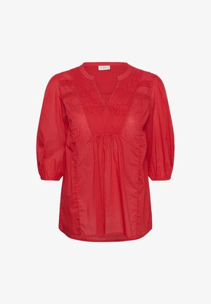 Raudona, laisvai krentanti palaidinė iš lengvos medžiagos. Turi V formos iškirptę, trumpas pūstines rankoves ir vertikalias klostes priekyje.