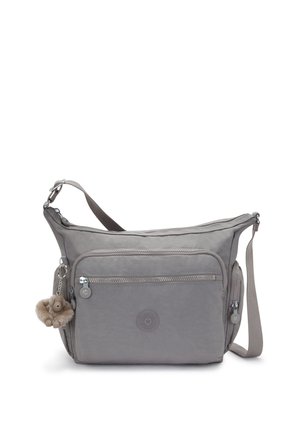 Grey fabric shoulder bag with a zippered front pocket, adjustable strap, and a fluffy charm keychain. Iconic logo embossed on the front.