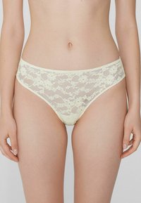 Culottes en dentelle jaune pâle, ornées de motifs floraux et dotées d'une taille élastique. Texture lisse avec un design semi-transparent.