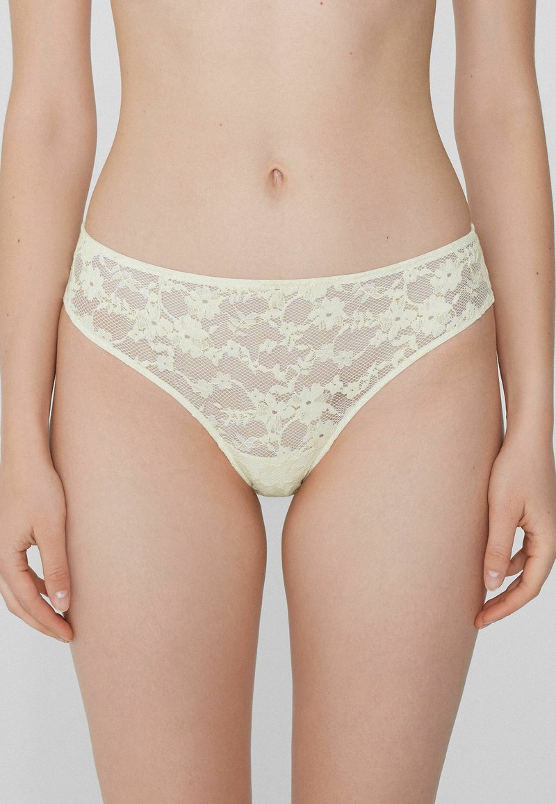 Culottes en dentelle jaune pâle, ornées de motifs floraux et dotées d'une taille élastique. Texture lisse avec un design semi-transparent.