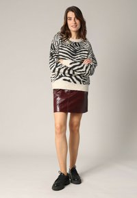 Pull noir et blanc à rayures zébrées en tissu tricoté, associé à une mini-jupe en cuir synthétique bordeaux. Des chaussures lacées noires complètent la tenue.