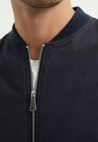 Veste bomber marine avec une fermeture éclair argentée et un col côtelé, dotée d'une fermeture éclair et d'un tissu doux et texturé.