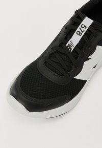Baskets noires de sport avec tige en maille, capuchon en caoutchouc et accents blancs. Comprend des lacets et une étiquette avec des chiffres sur la languette.