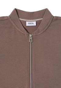 Bruine ribbelige jack met rits en opstaande kraag, voorzien van een zilveren rits en een label met de tekst "CECIL" binnenin de kraag.