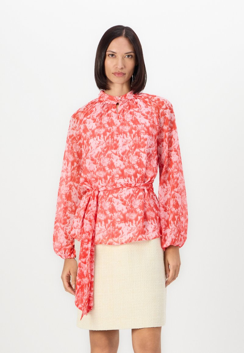 Lett, langermet bluse i rødt og rosa blomstermønster, med en nøkkelhulldesign og et selvbindende belte i midjen.