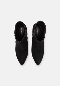 Botas de tobillo de ante negro con puntera afilada, que presentan un diseño minimalista y laterales cortados para un detalle adicional. Logo dorado en el interior.