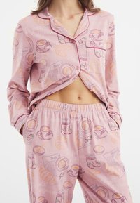 Pinker Schlafanzug mit einem Muster aus Frühstücksartikeln wie Croissants und Tassen. Aus weichem Stoff gefertigt, mit einem klassischen, lockeren Schnitt und Knopfdetails.