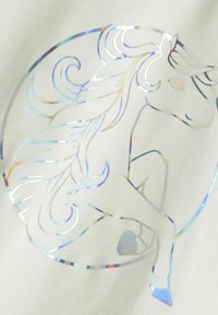 Una tela blanca presenta un diseño de unicornio holográfico, con detalles de melena fluida y un contorno circular, creando un efecto brillante y reflectante.