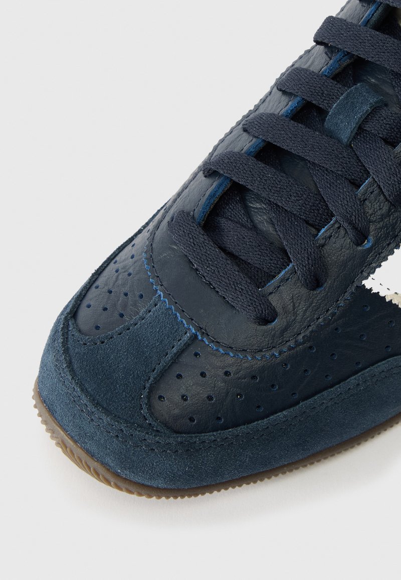 Marineblauwe sneaker met een mix van gladleer en suede, voorzien van geperforeerde details, platte veters en een gumrubberen zool.