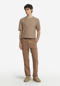 Brun kortærmet skjorte, afslappet pasform, parret med lysebrune cargo-bukser med lommer; beige slip-on sko fuldender looket.