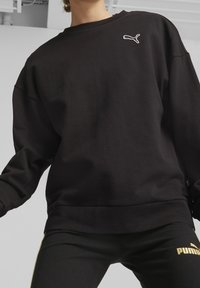 Felpa nera con scollatura a girocollo, vestibilità oversize e logo Puma bianco minimale sul petto. Texture morbida, finitura opaca.