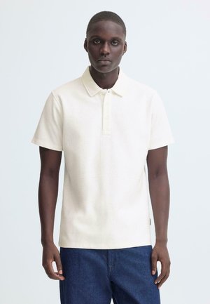 Poloshirt met korte mouwen in off-white stof, met een klassieke kraag, twee knopen en een losse pasvorm. Draagt met donkerblauwe spijkerbroek.