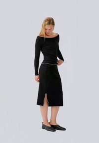 Top negru cu mânecă lungă și design off-shoulder, asociat cu o fustă neagră până la genunchi cu o fanta și margine cu dantelă. Pantofi negri cu talpă joasă.