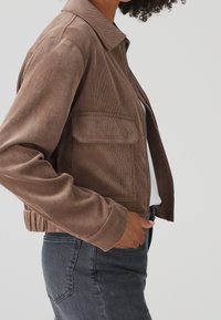 Brown corduroy jacket with a collared neckline, front zipper, and two chest pockets, featuring a cropped design and ribbed hem.