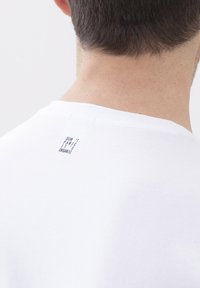 Witte biologische katoenen t-shirt met een ronde hals. Voorzien van een klein zwart geprinte label op de achterkant met de tekst "PANIEK NIET, HET IS BIOLOGISCH."