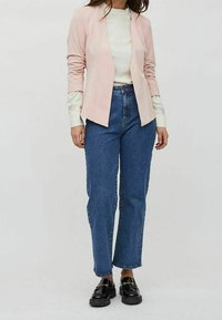 Ljusrosa skräddarsydd blazer med långa ärmar, tillsammans med en vit topp och högmidjade blå jeans. Svarta snörskor fulländar outfiten.