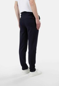 Marineblå joggebukser med elastisk liv, slim fit og to baklommer. Har en liten rød logo på venstre lomme.