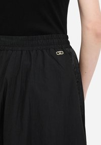 Pantaloncini neri leggeri con vita elastica, texture liscia e dettaglio logo dorato sul lato.