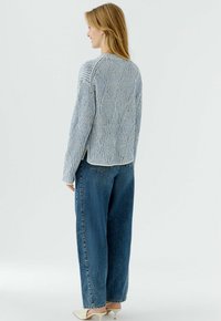 Lichtblauwe gebreide trui met een getextureerd diamantpatroon, gecombineerd met donkerblauwe high-waist denim jeans. Heeft een wijd gesneden ontwerp en verlaagde schouders.