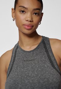 Szary sportowy top na ramiączkach o teksturowanym wykończeniu, prążkowanym dekolcie i z nadrukowanym logo. Posiada czarne przeszycia akcentujące na ramionach.