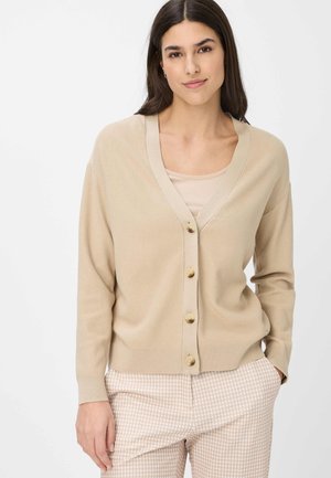 Beige knitted cardigan with a deep V-neck, button front, and ribbed cuffs. Light, textured fabric complements cream-colored top and patterned trousers.