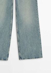 Jean en denim bleu clair à jambe droite, présenté de mi-cuisse vers le bas, avec un léger délavage et des ourlets cousus sur fond blanc.