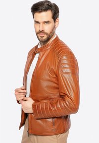 Braune Lederjacke mit gerippten Schulterausschnitten, einem Druckknopfkragen und seitlichen Reißverschlusstaschen; glatte Textur und taillierte Passform.