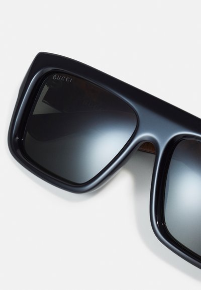 Occhiali da sole rettangolari neri con lenti a gradiente scuro. La montatura in plastica spessa presenta una finitura liscia. Il logo "Gucci" è impressa sulla tempia.