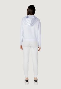 Felpa bianca con cappuccio e coulisse, abbinata a pantaloni slim-fit bianchi e scarpe con zeppa. Texture liscia, design minimalista e nessun motivo visibile.