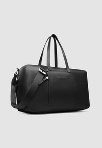Sac de voyage noir en matériau lisse. Il dispose de deux poignées supérieures, d'une bandoulière amovible et présente un design minimaliste sans motifs.