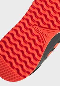 Suola delle calzature Adidas con un design in gomma rossa texturizzata, caratterizzata da motivi a onda continui e un logo impresso al centro.