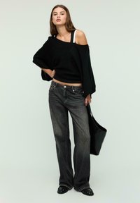 Pull noir surdimensionné avec une épaule dénudée, associé à un jean évasé gris foncé et un sac noir. Accessoirisé avec des chaussures plates noires.