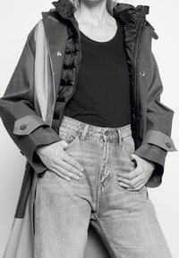 Grå och svart jacka med pösig foder, svart linne, och ljusblå jeans med hög midja. Jackan har knappar och kragedetaljer.